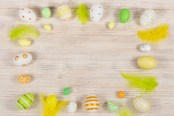 Easter frame with eggs and feathers on a light wooden background. Minimal concept. View from above. Card with copy space for text.