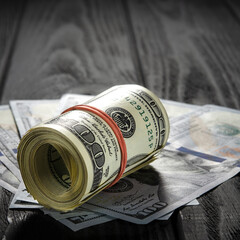 A thick roll of old hundred dollar banknotes tied a red rubber band lies on the whisker of new hundred dollar bills