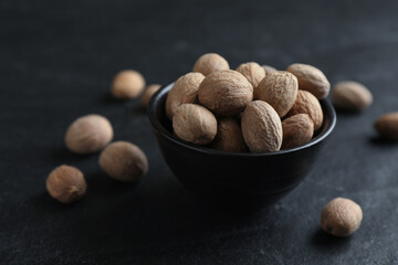 Bowl with nutmeg seeds on black table, closeup