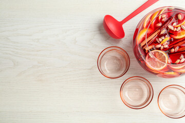 Bowl of delicious aromatic punch drink, ladle and empty glasses on white wooden table, flat lay. Space for text