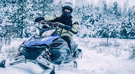 Fotobehang Man driving snowmobile in snowy forest. Man on snowmobile in winter mountain. Snowmobile driving © Yevhen