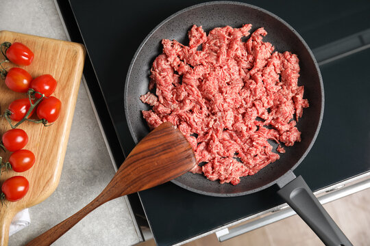 Frying pan with raw minced meat on induction stove indoors, flat lay