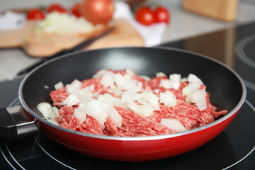 Frying pan with raw minced meat and chopped onion on induction stove, closeup