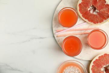 Glasses of pink pomelo juice with straws and fruit on white marble table, flat lay. Space for text