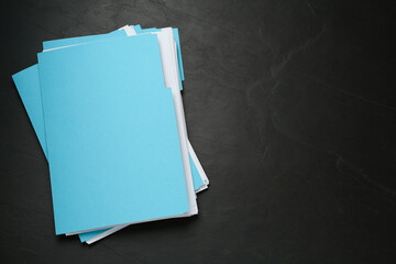 Turquoise files with documents on black slate table, top view. Space for text