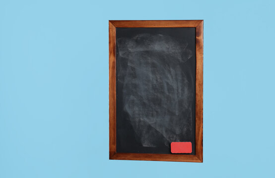 Dirty black chalkboard with duster on light blue background