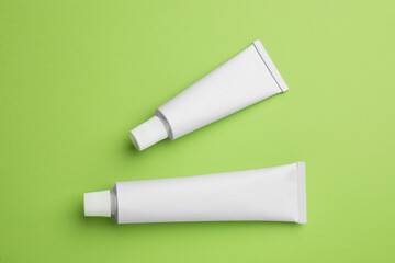 Blank white tubes of ointment on light green background, flat lay. Space for text