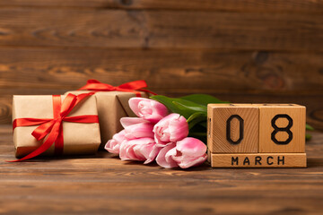 International Women's Day. Beautiful postcard for March 8. Bouquet of pink tulips with gift on brown textured wood. Holiday concept. Copy space. Side view.