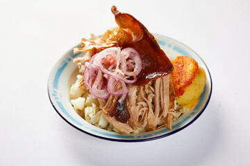 Hornado, a typical Ecuadorian dish that consists on pork cooked on firewood. It’s accompanied by llapingacho and mote. Served on a small plate on a white background. 