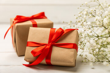 Gift box wrapped in kraft paper and delicate gypsophila flowers on a white textured wood.Holiday concept. Place for copy. Place for text. Side view.