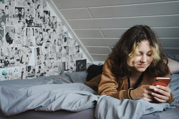 Teenager Mädchen liegt auf dem Bett mit Handy und schreibt eine Nachricht