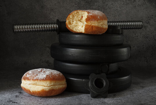 Dumbbells barbell weight plates and Polish pączki deep-fried doughnuts. Fat Thursday (Tłusty czwartek). Pączek, traditional feast day in Poland. Fitness gym workout, cheat day vs sticking to diet.
