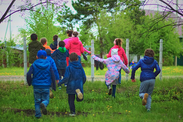 Rear view of happy kids running around in spring nature. Green grass. Games in the park. Selective focus.
