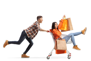 Young man pushing a young female sitting inside a shopping cart and holding shopping bags