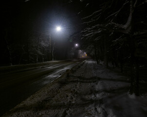 Night street covered with snow, illuminated by lanterns goes into the distance