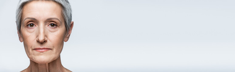 close up of mature woman with grey hair looking at camera isolated on grey, banner