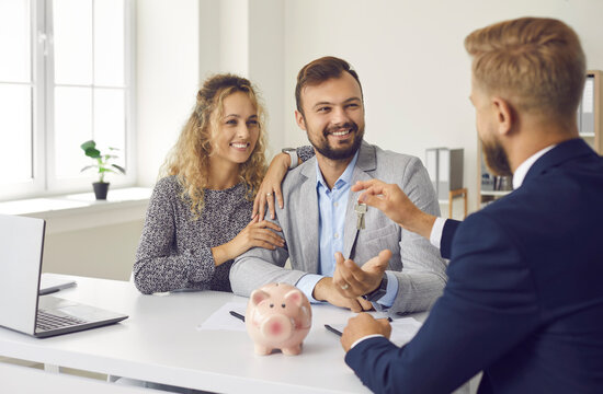 Happy young family signs contract in office and receives keys from real estate agent. Meeting in office of realtor and couple who decided to buy their first home. New beginning concept.