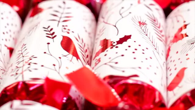 Red and white christmas crackers with robin, holly, tree and swirl pattern on a wooden table slow motion diagonal tracking shot