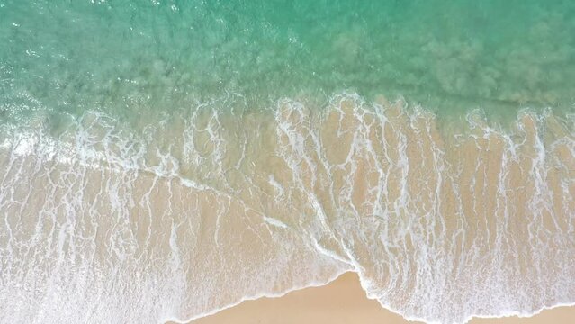 aerial top view sea waves seamless loop on the white sand beach. .Wave after wave swept towards the shore. .green sea, white bubble waves,and clear sand landscape. Paradise beach.