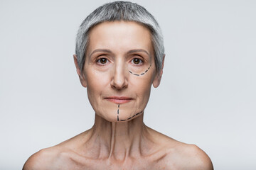 mature woman with grey hair and marked lines on face looking at camera isolated on grey