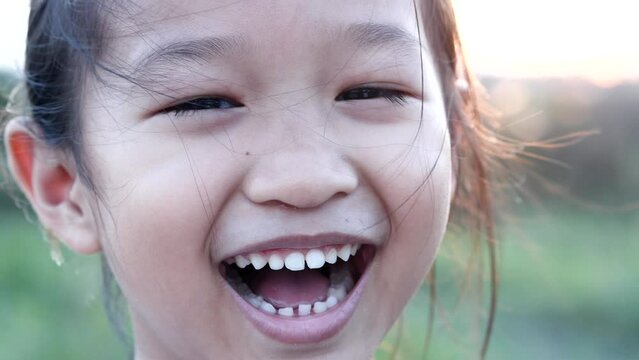 Portrait happy Asian little child girl smiling, laughing, looking at camera with beautiful sunset or sunrise in summer or spring nature outdoor background. Concept of portrait, happy children, family.