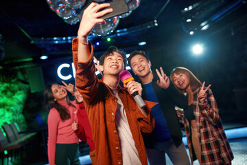 Singing into microphone and making selfie at karaoke party in club
