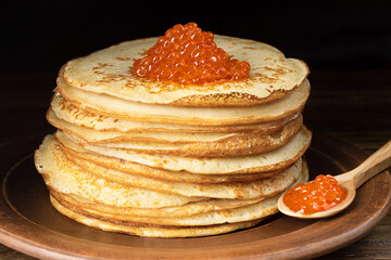 Pancakes with red caviar. Lots of pancakes. Pancakes on a plate and a wooden spoon. Close-up. Selective focus.