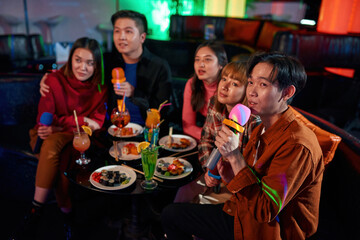 Cheerful asian friends laughing and singing songs at karaoke club