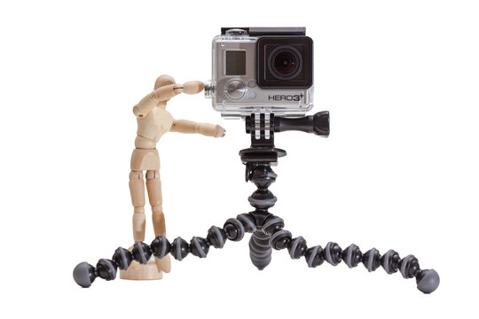 Wooden mannequin taking photos with GoPro Hero 3+ camera on GorillaPod tripod on white background.