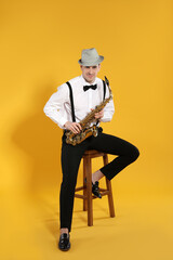 Naklejka premium Young man in elegant outfit with saxophone on yellow background