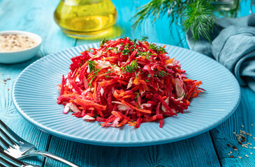 Salad with beets, carrots and cabbage seasoned with parsley and sesame seeds close-up on a blue background.