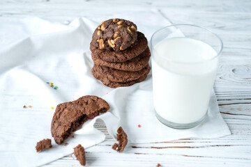 a glass of milk and chocolate chip cookies on a white wooden background