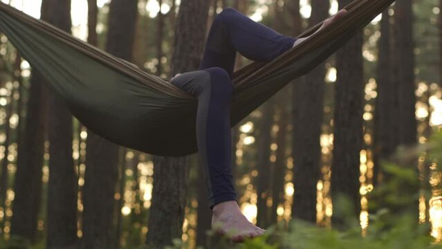 A happy girl is resting in a summer forest on a green hammock