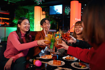 Cheerful asian friends clinking glasses above table at nightclub