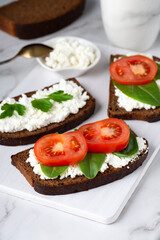 Fototapeta na wymiar Slice of rye bread with cottage cheese and tomatoes on a wooden cutting board on a white background