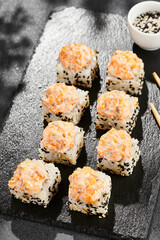 Baked Maki sushi on dark slate. Hot sushi roll with salmon and cheese. Sushi roll sesame outside, baked salmon and cheese topped. Style concept japanese menu with black background, leaves and shadow.
