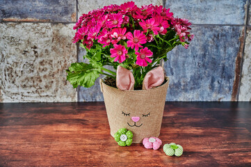 Flower pot with a rabbit face and small fabric flowers in focus.