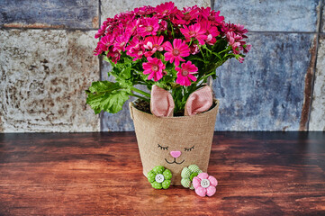 Flower pot with a rabbit face and small fabric flowers in focus.