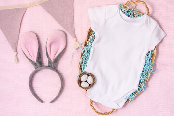 Easter mockup baby bodysuit with bunny and easter eggs on pink cover background. Flat lay, top view, copyspace.