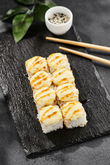 Baked Maki sushi on dark slate. Hot cheese maki with unagi sauce. Sushi roll with baked cheese and unagi sauce topped. Style concept japanese menu with black background, leaves and hard shadow.
