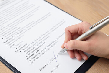 Woman signing contract at wooden table, closeup.