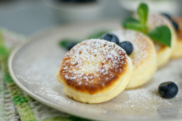 Cottage cheese pancakes with sour cream, raspberries, blueberries and mint, homemade traditional Ukrainian and Russian syrniki on rustic wooden background. Top view.