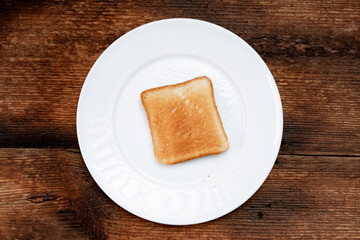 A piece of toasted white toast on a white plate. Dark wooden background. Minimalism. Food concept. Top view.