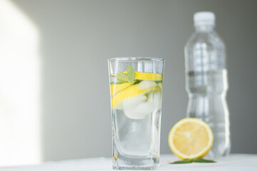 glass of water with lemon and ice and mint on blue background and white table