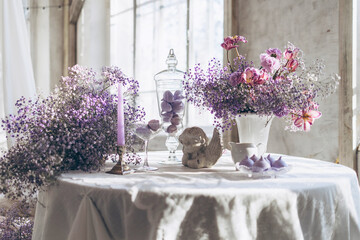 table set in lilac tones very peri color of the year 2022 with candle, statuette angel, purple marshmallow, butterfly and lilac gypsophila flowers, vintage decor in retro loft style room, celebration