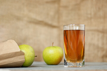 Glass of apple juice with apples on a wooden table, close-up.
