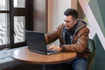 A young man uses a laptop while sitting in a cafe. Freelance. Remote work. Global communications.