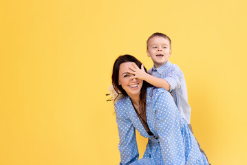 Adorable little boy is playing with his mom. Happy family mother and cute little boy son on yellow background having fun enjoying sweet moments together