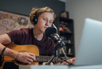 Home sound studio young teenager portrait playing guitar in Headphones recording voice music using...