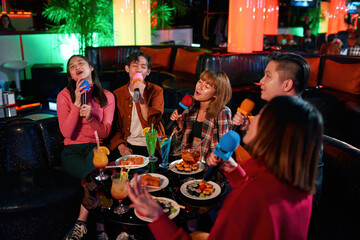Group of asian friends having fun and singing songs at karaoke club